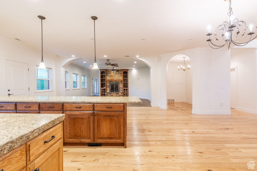 Kitchen featuring hanging light fixtures, light stone countertops, ceiling fan with notable chandelier, crown molding, and light hardwood / wood-style floors