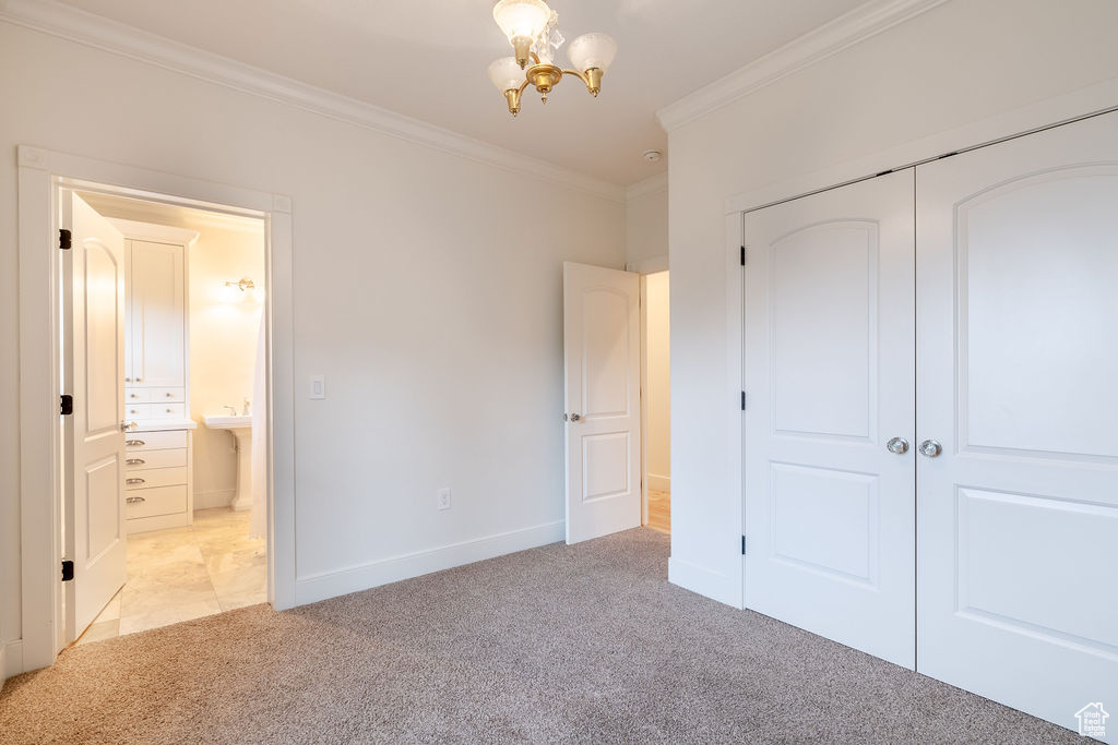 Unfurnished bedroom with crown molding, an inviting chandelier, light carpet, and a closet