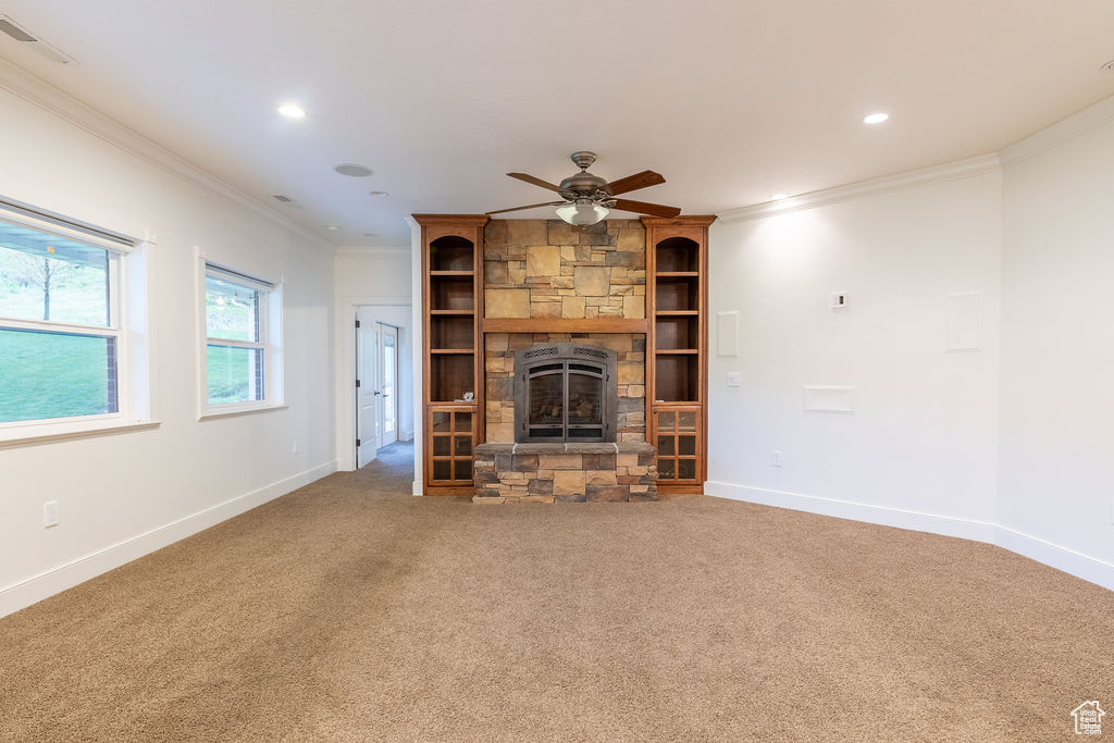 Unfurnished living room featuring a fireplace, carpet floors, ceiling fan, and crown molding