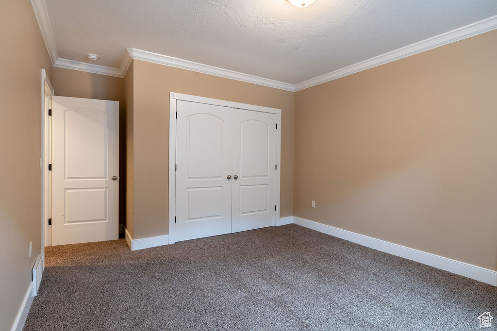 Unfurnished bedroom with dark colored carpet, crown molding, a closet, and a textured ceiling