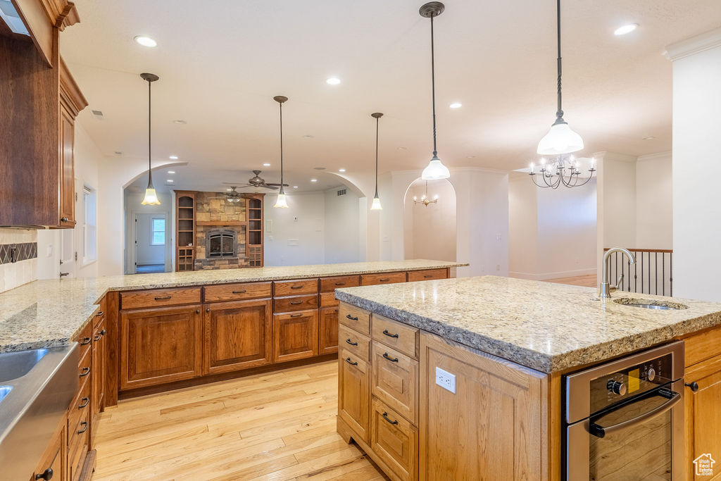 Kitchen with pendant lighting, light wood-type flooring, a kitchen island, and light stone countertops