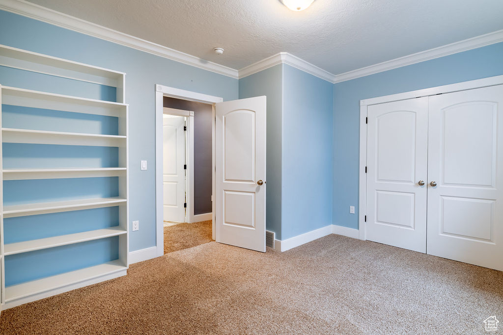 Unfurnished bedroom with light colored carpet, a textured ceiling, crown molding, and a closet