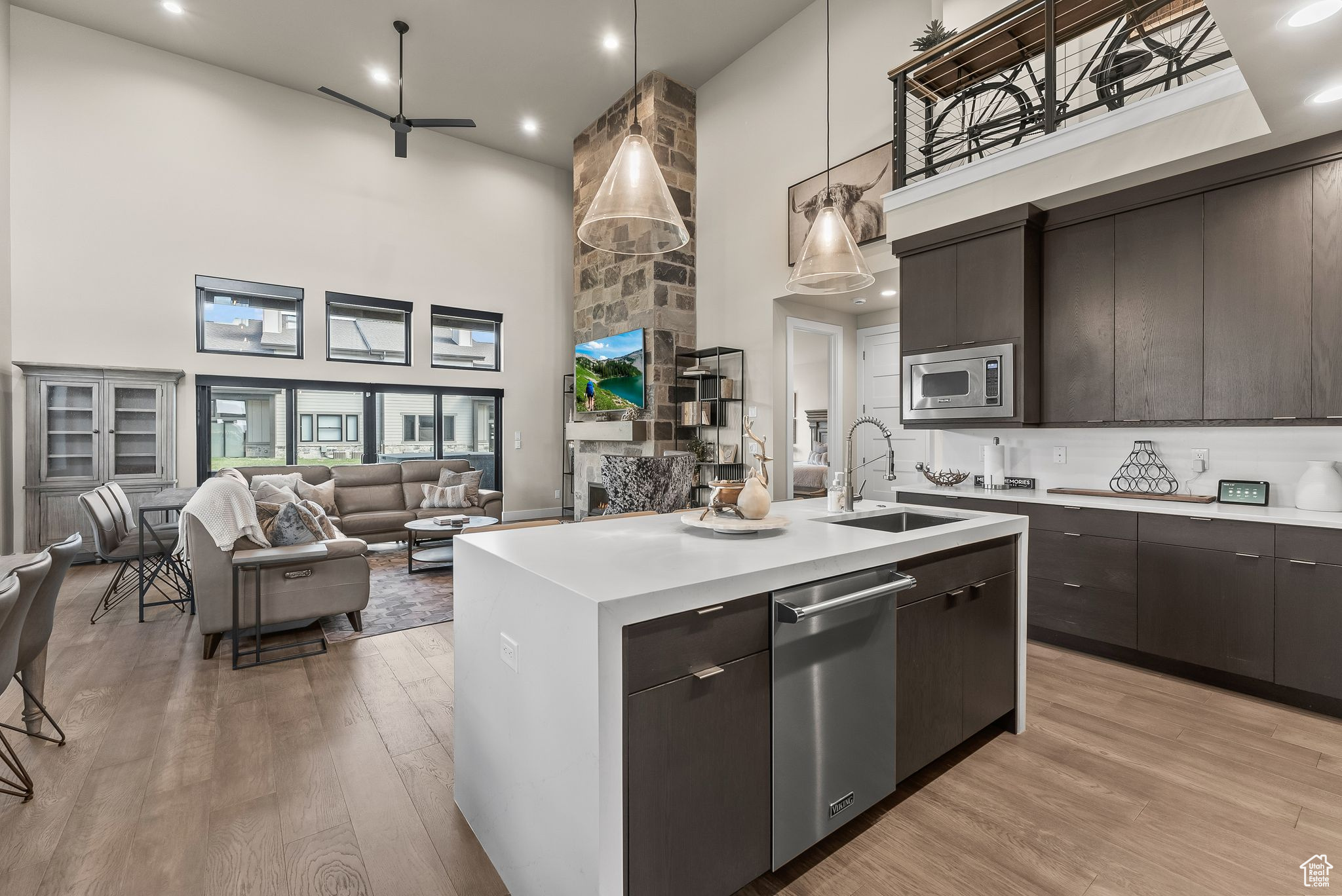 Kitchen with hanging light fixtures, a high ceiling, stainless steel appliances, light hardwood / wood-style flooring, and a kitchen island with sink