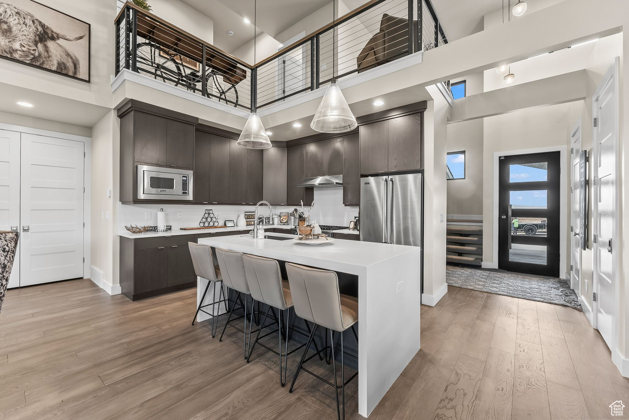 Kitchen with stainless steel appliances, a towering ceiling, light wood-type flooring, and a kitchen island with sink