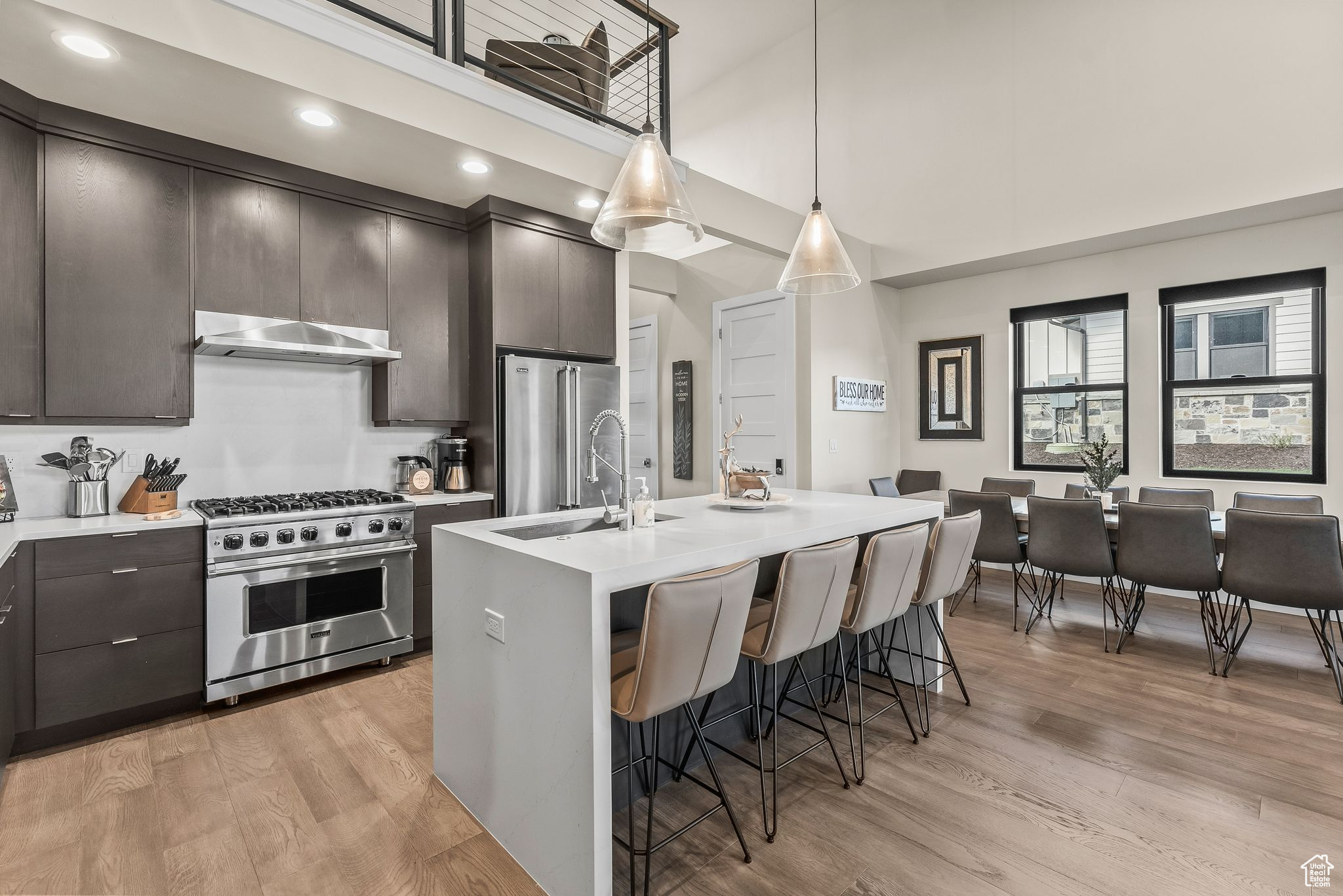 Kitchen featuring high end appliances, pendant lighting, light hardwood / wood-style floors, and a kitchen island with sink