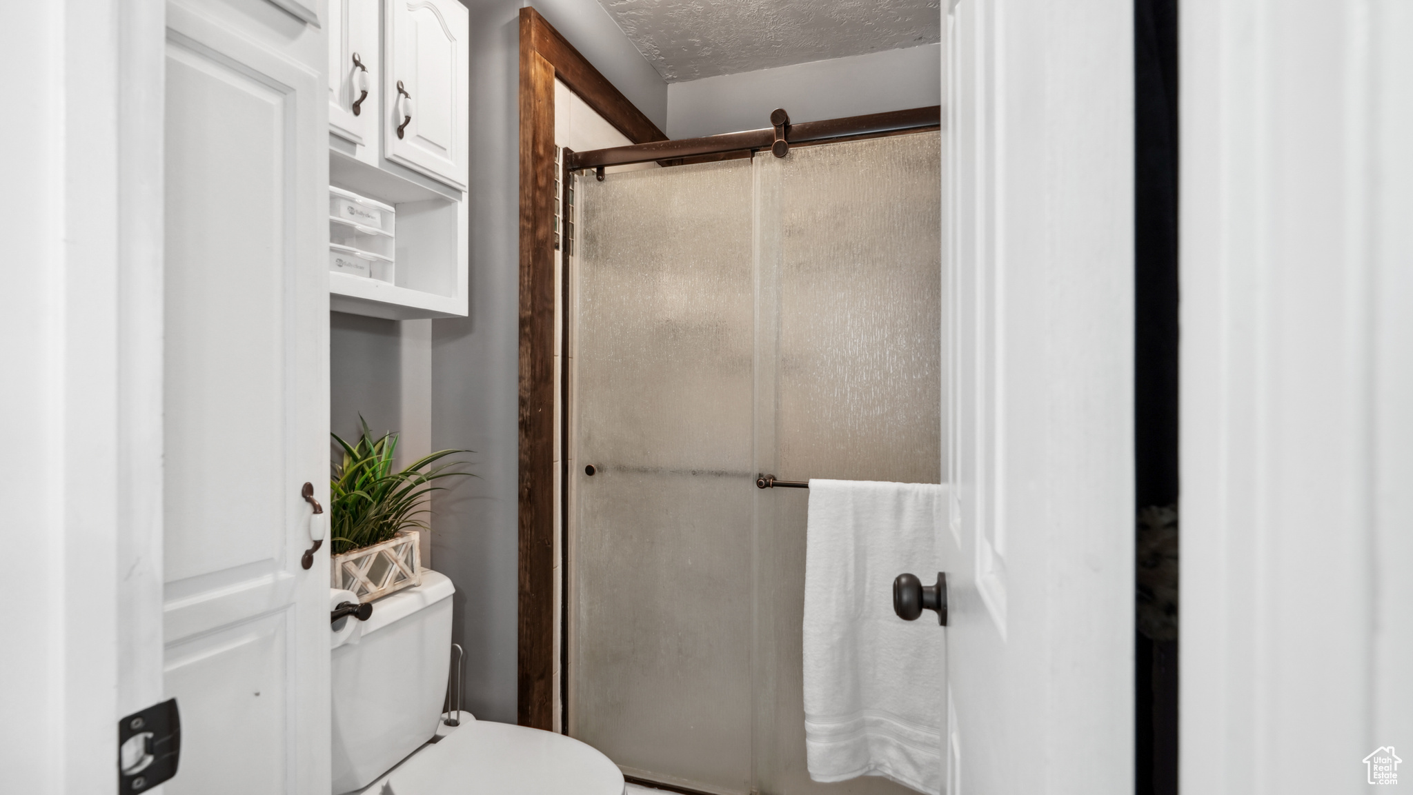 Primary bathroom with a textured ceiling, an enclosed shower, and toilet