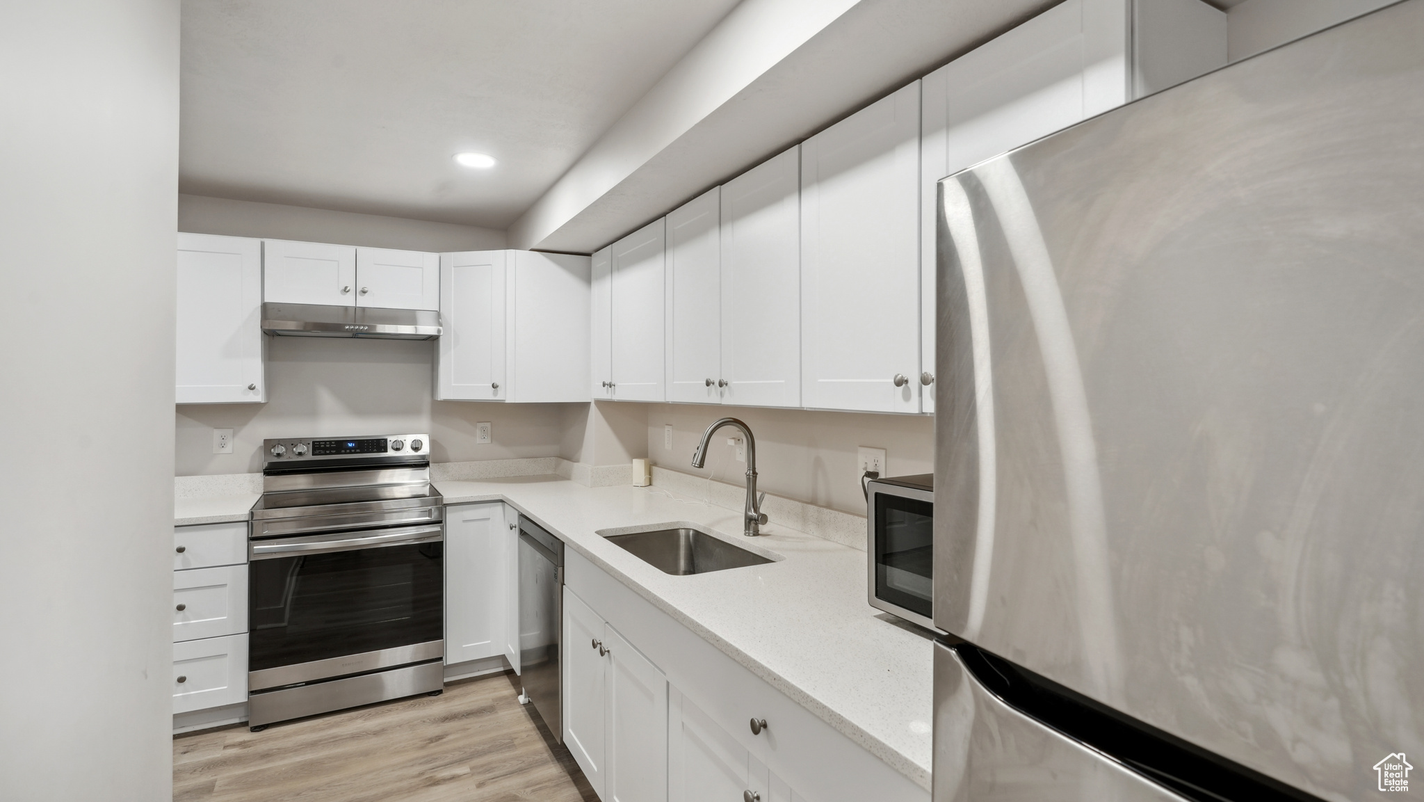 Kitchen featuring white cabinets, light hardwood / wood-style flooring, appliances with stainless steel finishes, sink, and light stone counters