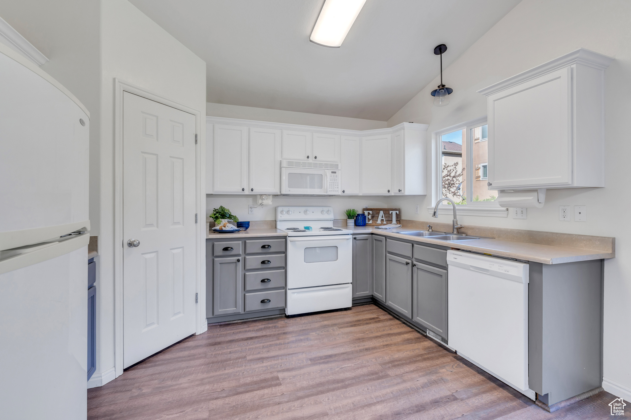 Kitchen with hardwood / wood-style flooring, gray cabinets, white appliances, and lofted ceiling