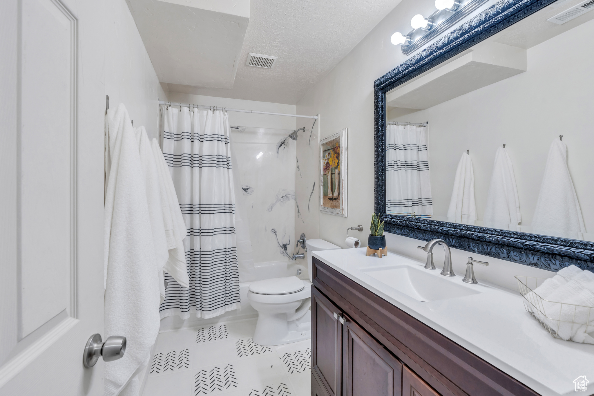 Full bathroom featuring a textured ceiling, oversized vanity, tile floors, toilet, and shower / bathtub combination with curtain