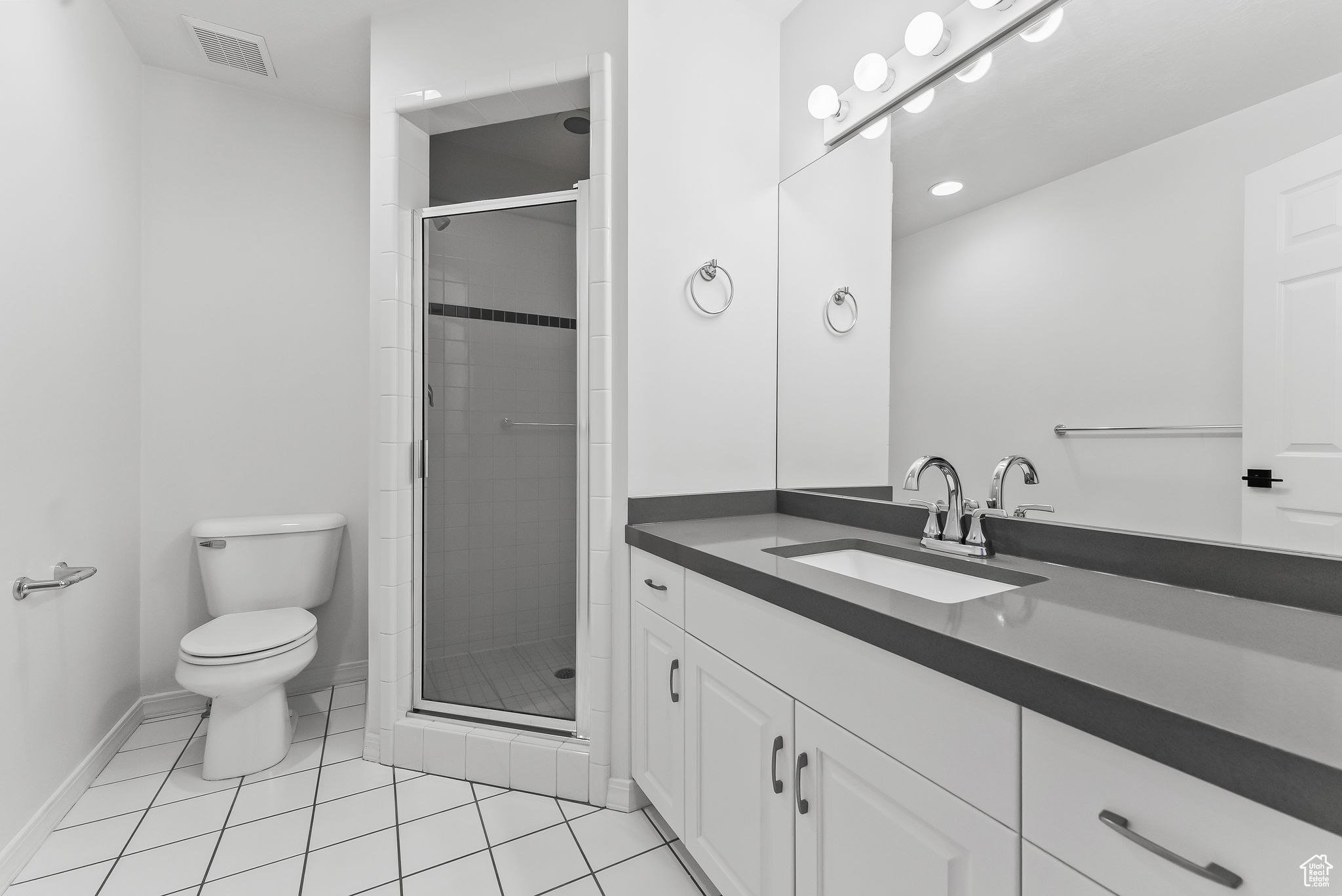 Bathroom featuring an enclosed shower, toilet, vanity with extensive cabinet space, and tile flooring