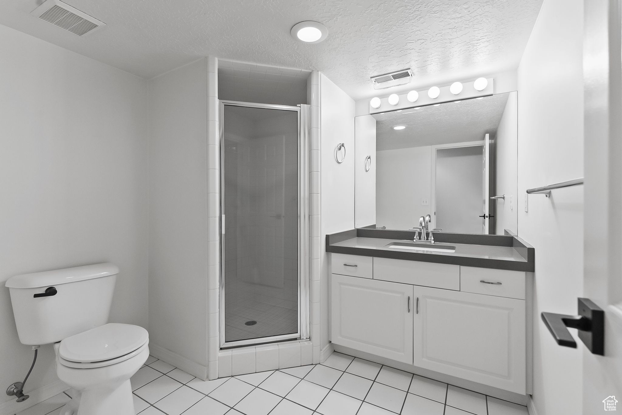 Bathroom featuring a shower with shower door, vanity, toilet, and tile flooring