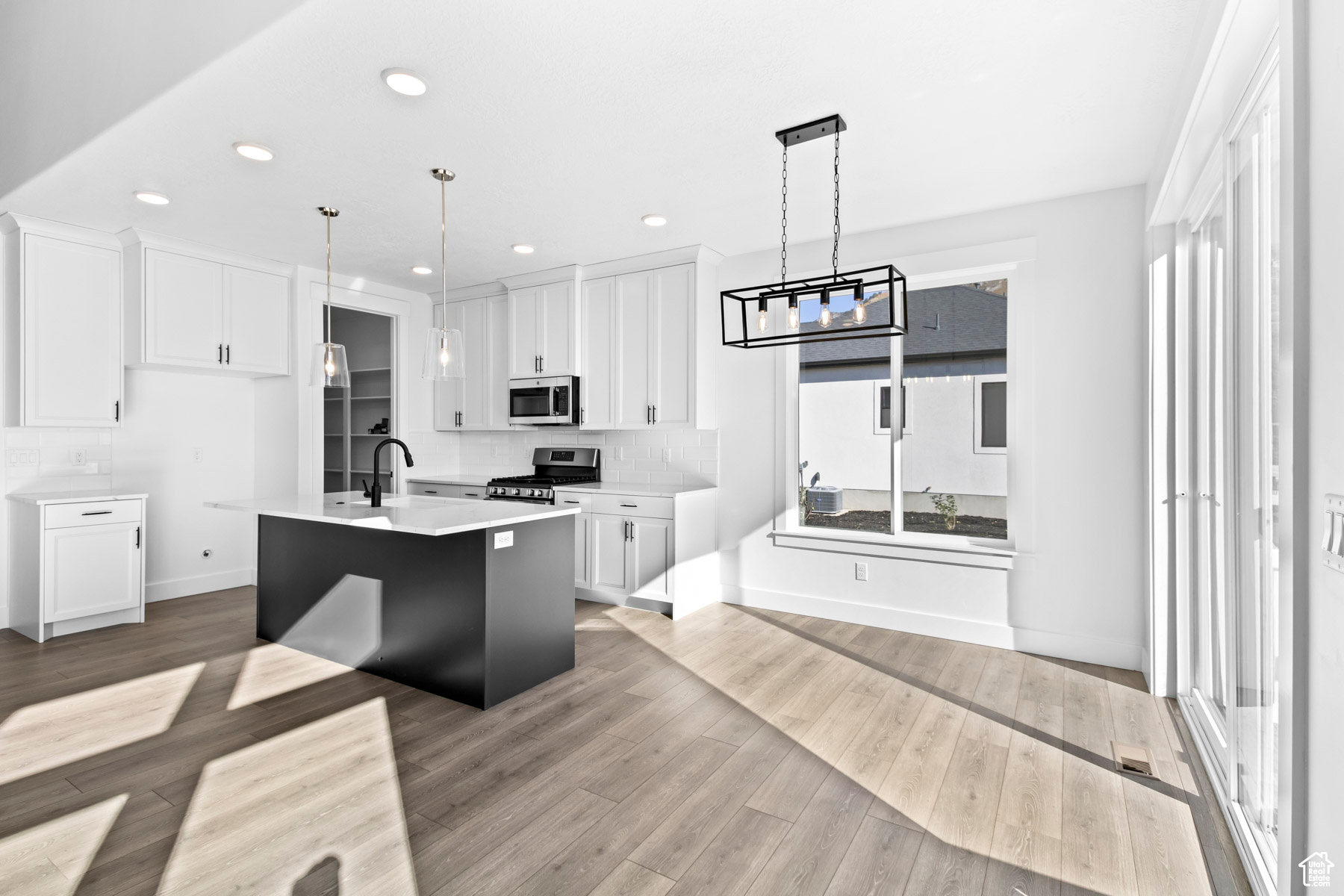 Kitchen featuring a kitchen island with sink, hanging light fixtures, light hardwood / wood-style flooring, white cabinetry, and appliances with stainless steel finishes