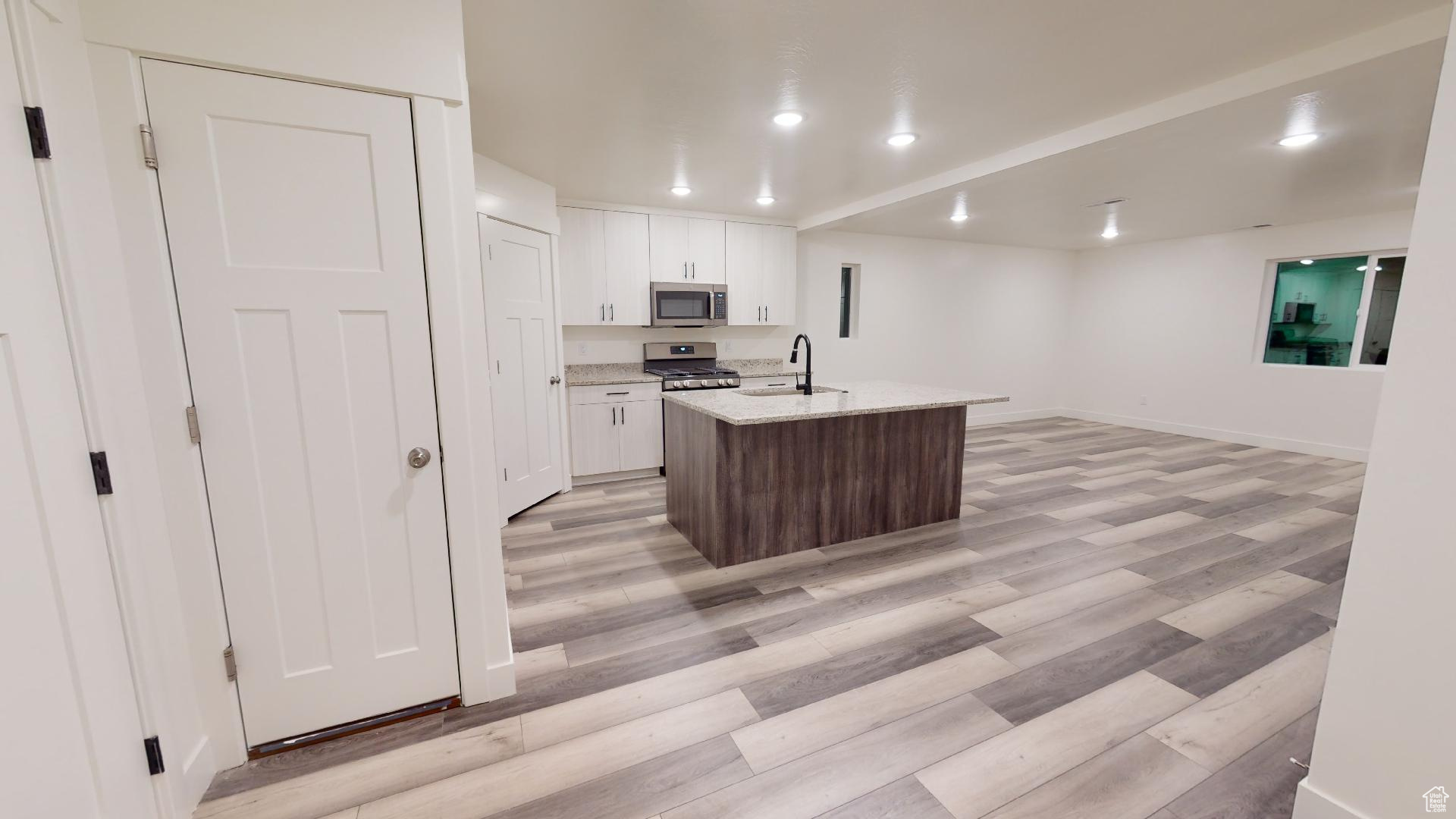 Kitchen with white cabinets, light hardwood / wood-style flooring, a center island with sink, and light stone countertops