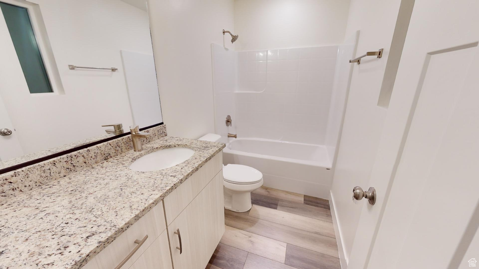 Full bathroom featuring washtub / shower combination, toilet, vanity with extensive cabinet space, and hardwood / wood-style flooring