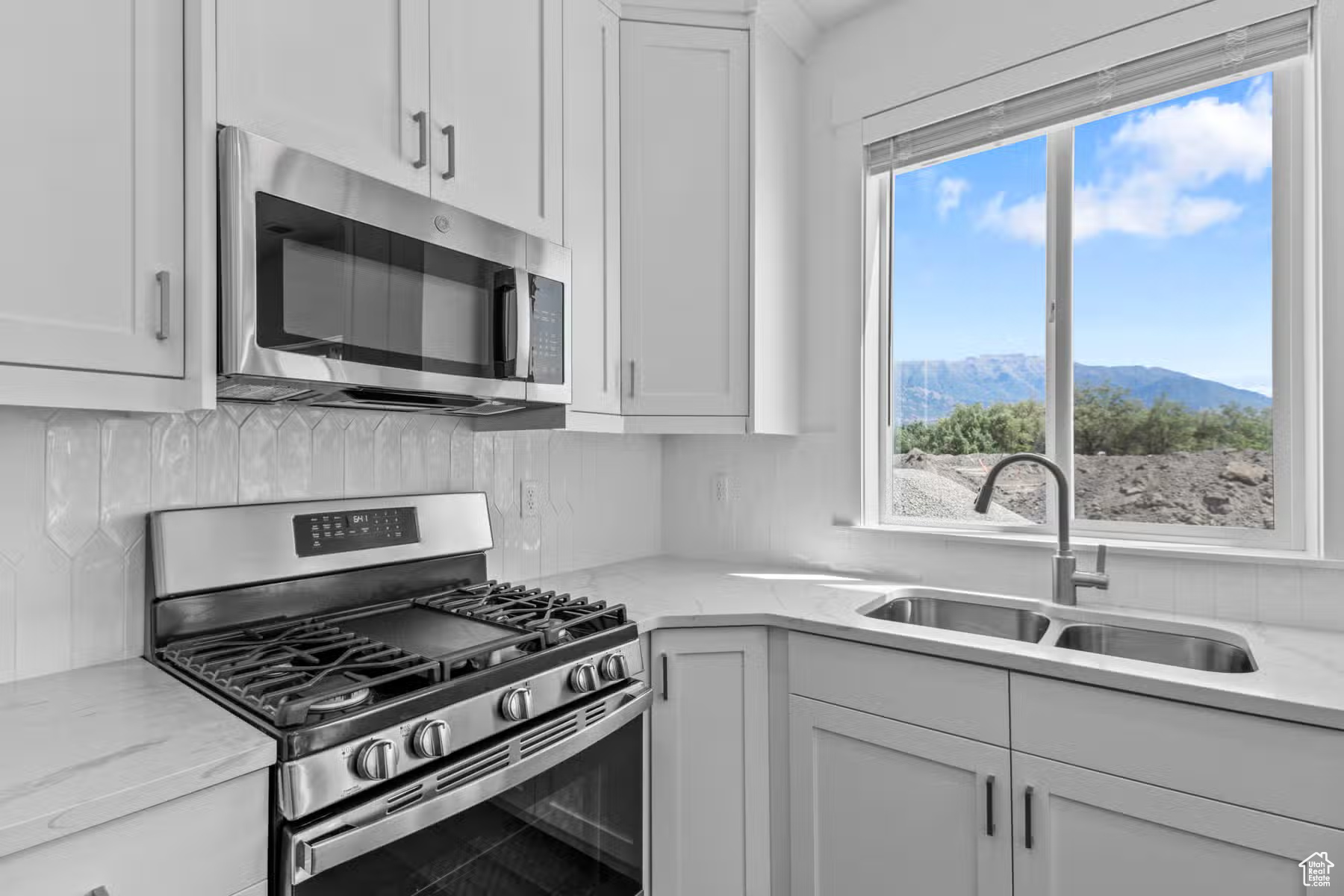 Kitchen with light stone countertops, appliances with stainless steel finishes, white cabinets, sink, and a mountain view