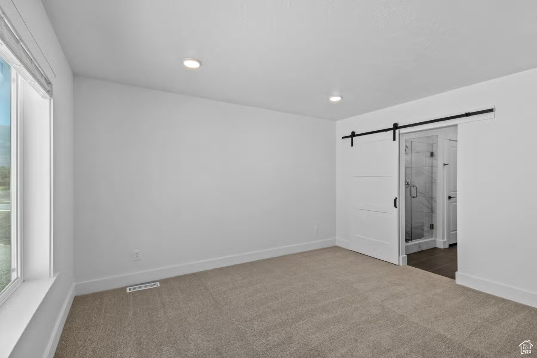 Unfurnished bedroom with dark colored carpet, ensuite bathroom, and a barn door