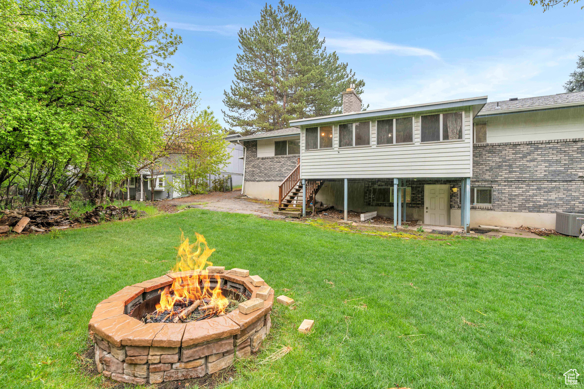 Back of property featuring 2 central AC units, an outdoor fire pit, and a luscious lawn