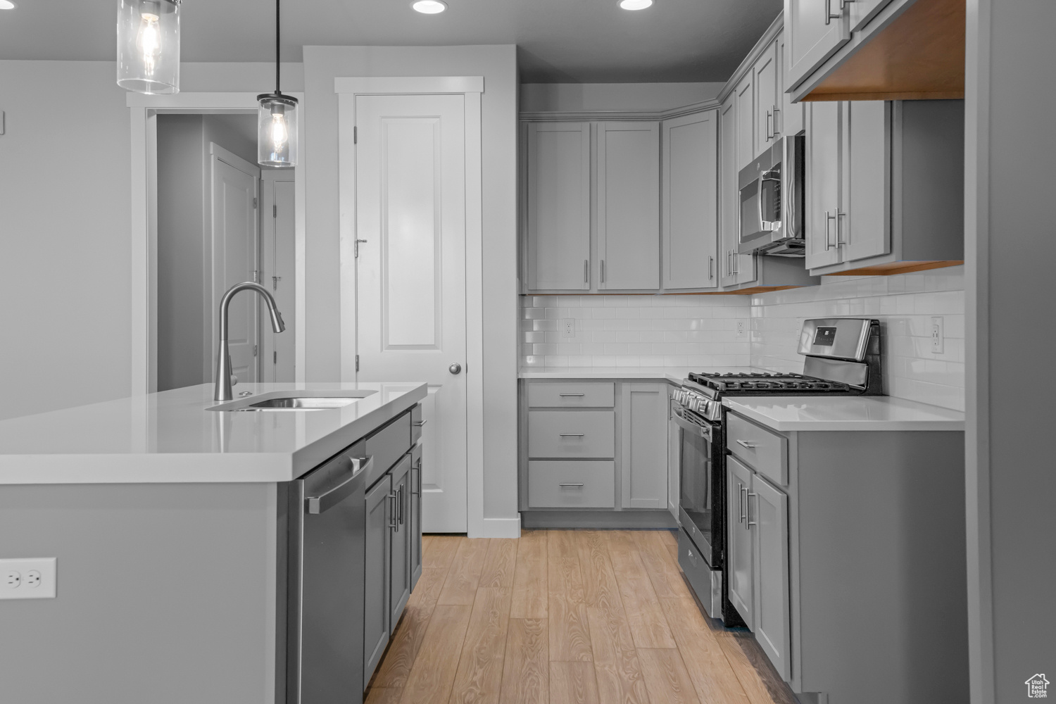 Kitchen featuring appliances with stainless steel finishes, sink, light hardwood / wood-style floors, gray cabinets, and a kitchen island with sink