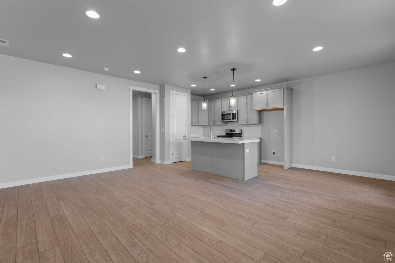 Kitchen with pendant lighting, light wood-type flooring, a kitchen island with sink, and stove