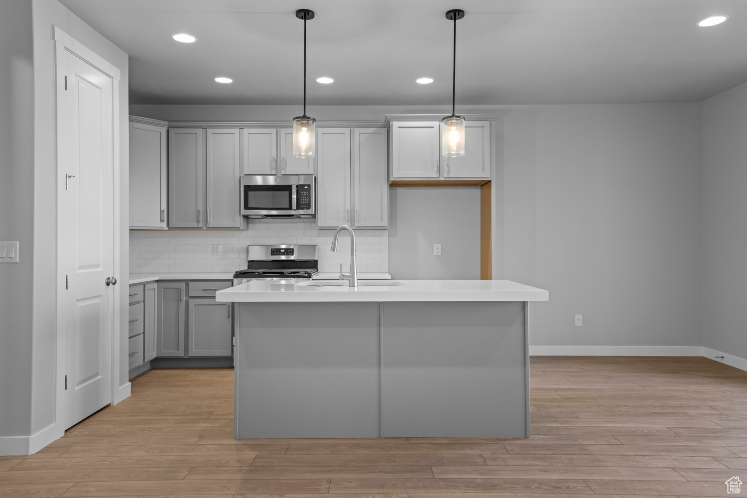 Kitchen with appliances with stainless steel finishes, light hardwood / wood-style floors, tasteful backsplash, a kitchen island with sink, and pendant lighting