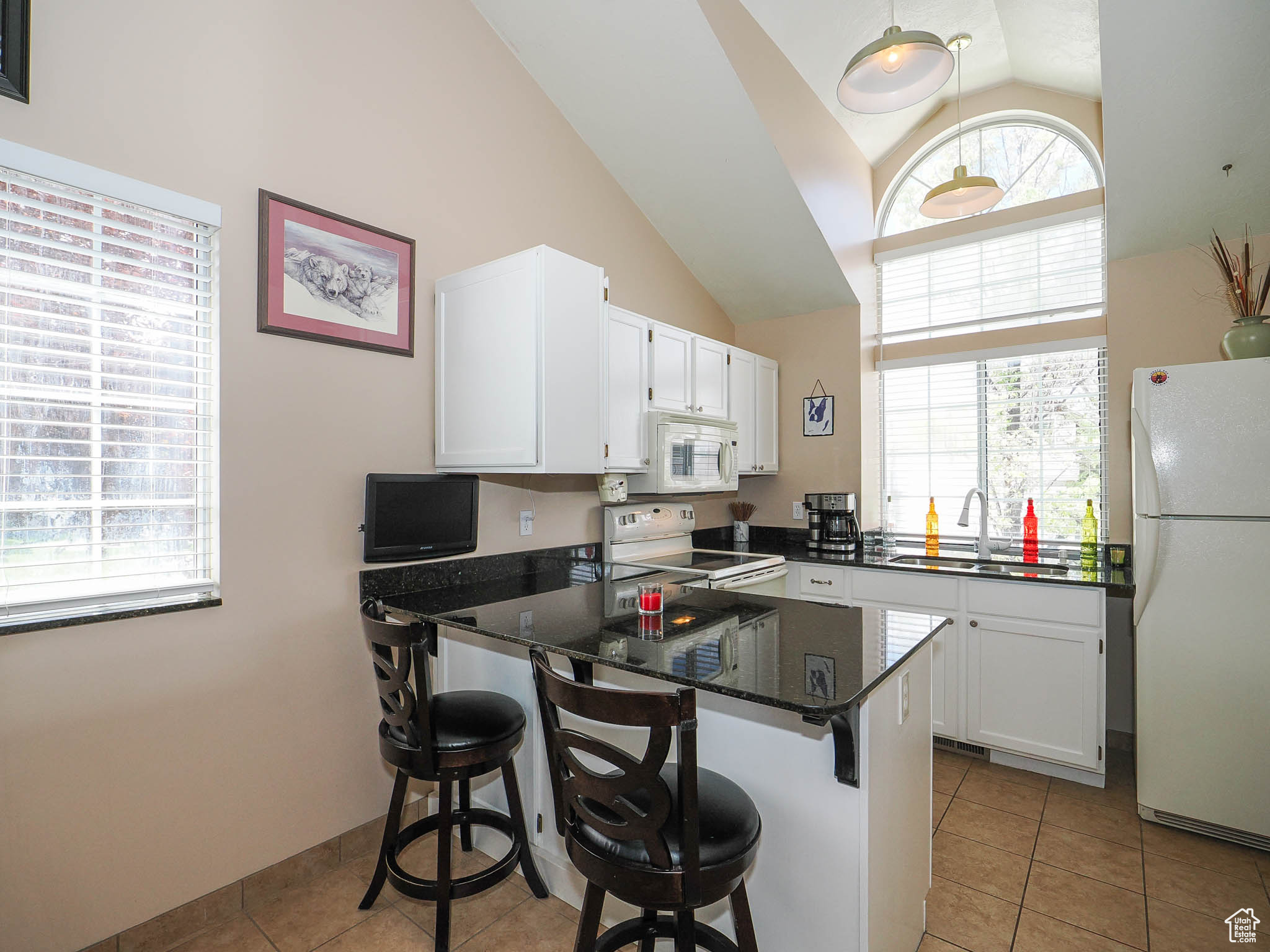 Kitchen featuring a kitchen bar, white cabinets, white appliances, and sink