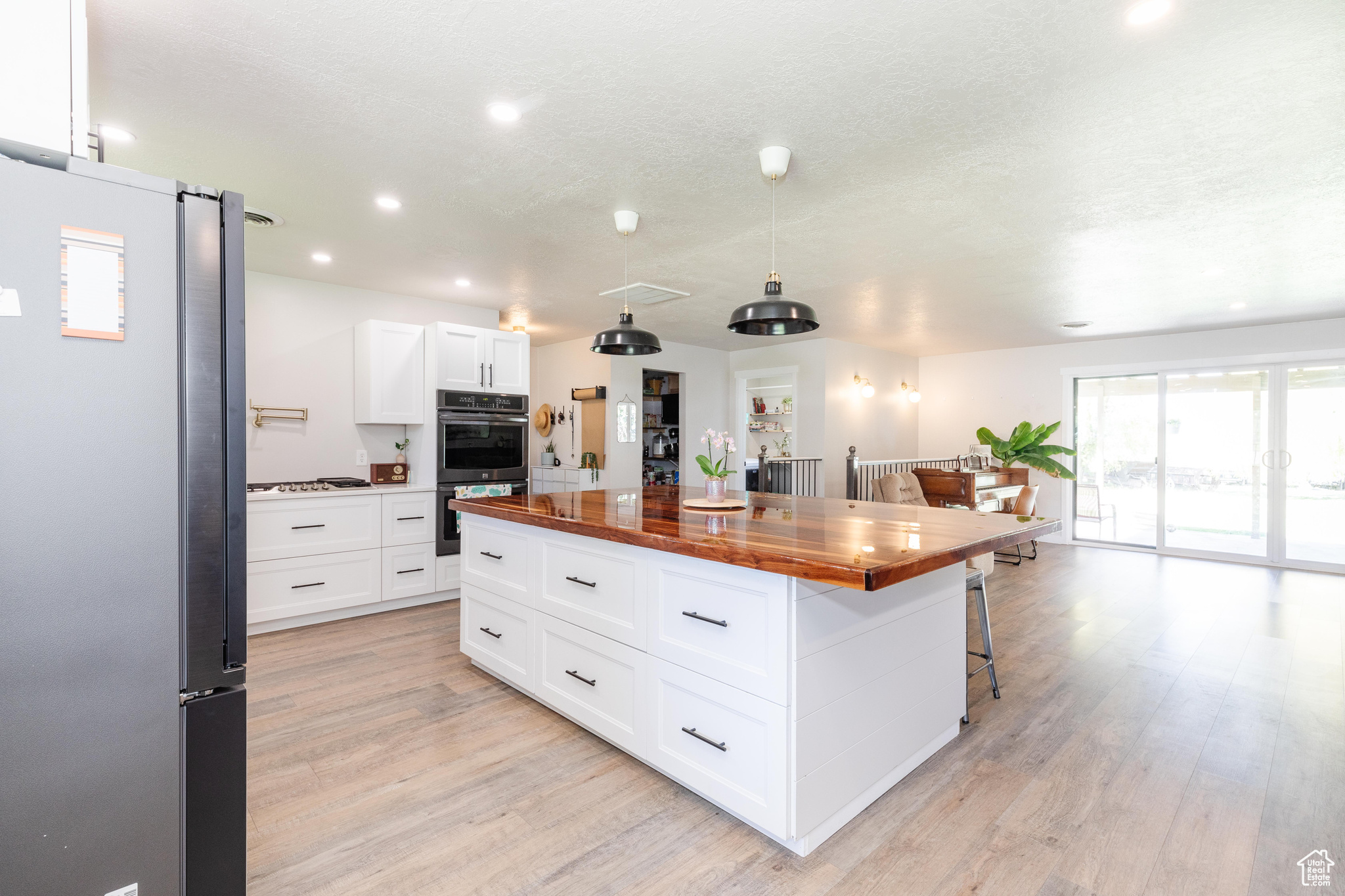 Kitchen with butcher block counters, a kitchen island, stainless steel appliances, white cabinets, and light wood-type flooring