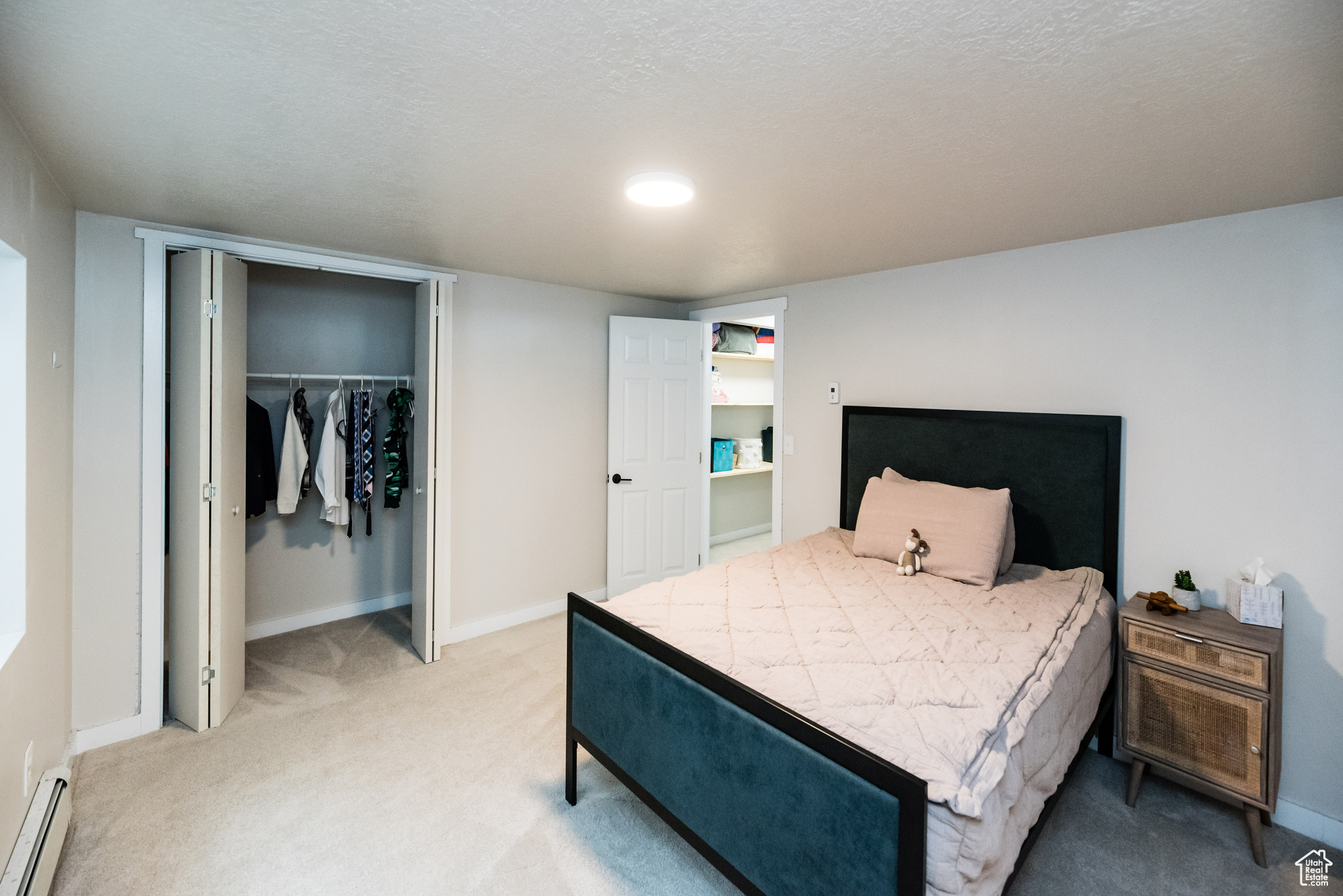 Carpeted bedroom with a closet, a baseboard heating unit, and a textured ceiling