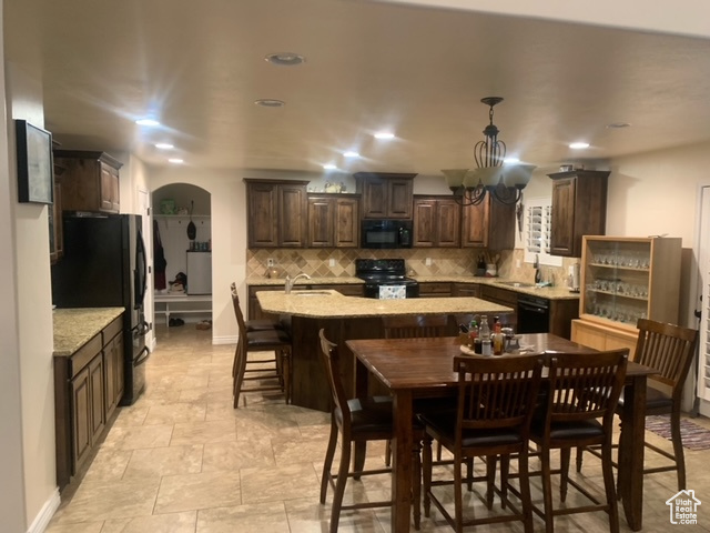 Kitchen featuring dark brown cabinets, light tile flooring, pendant lighting, and black appliances
