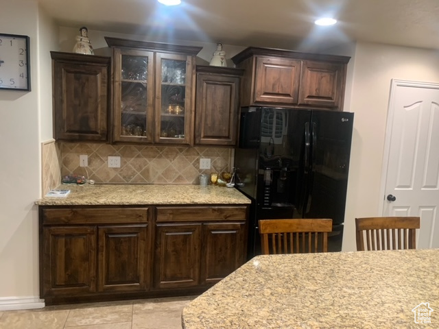 Kitchen with backsplash, dark brown cabinets, black fridge, and light tile floors