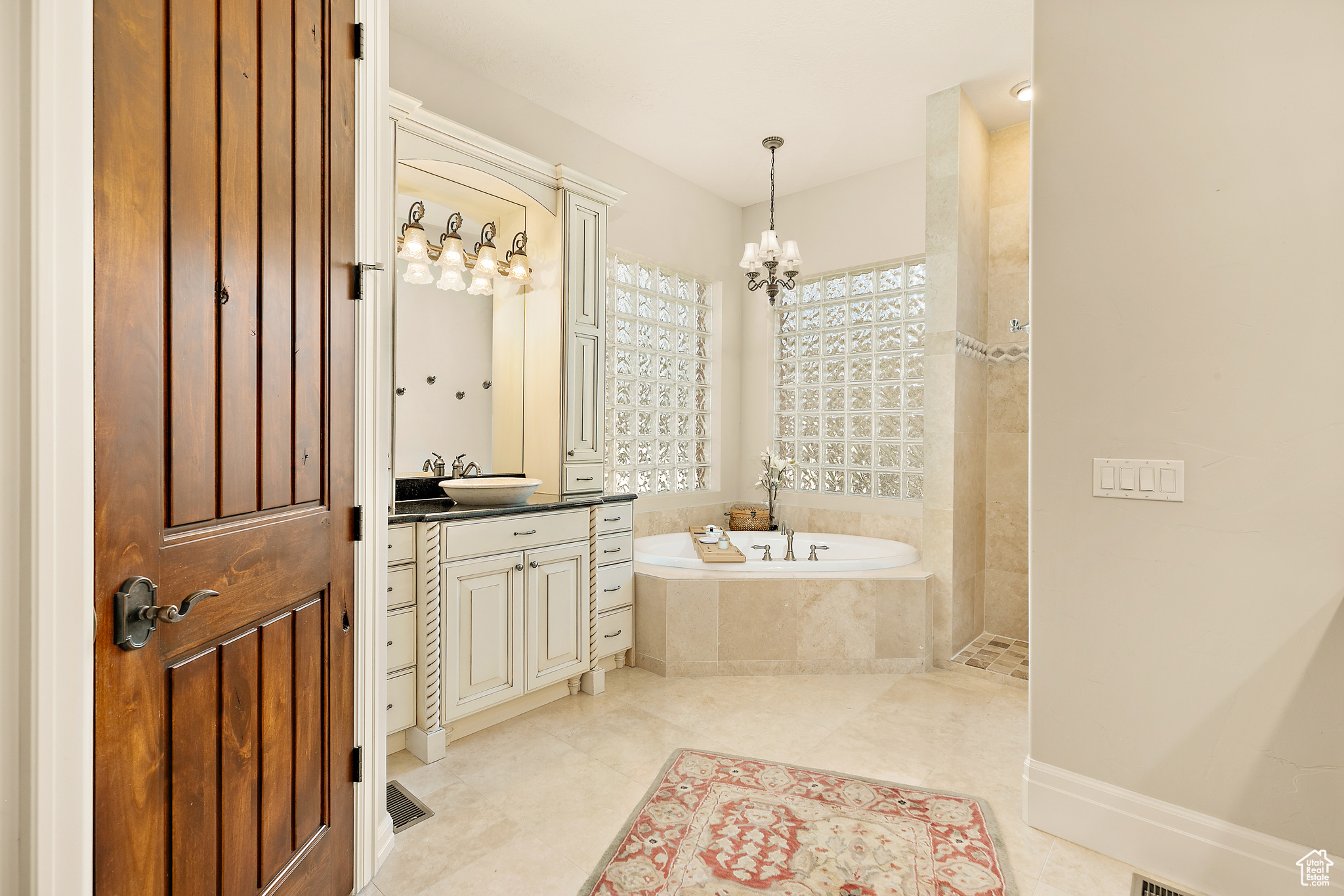 Bathroom with a relaxing tiled bath, tile floors, vanity, and a notable chandelier