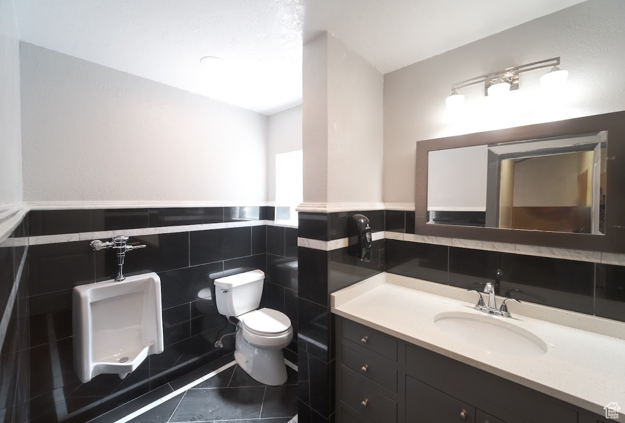 Mens Bathroom with tile walls, backsplash, toilet, vanity, and tile floors
