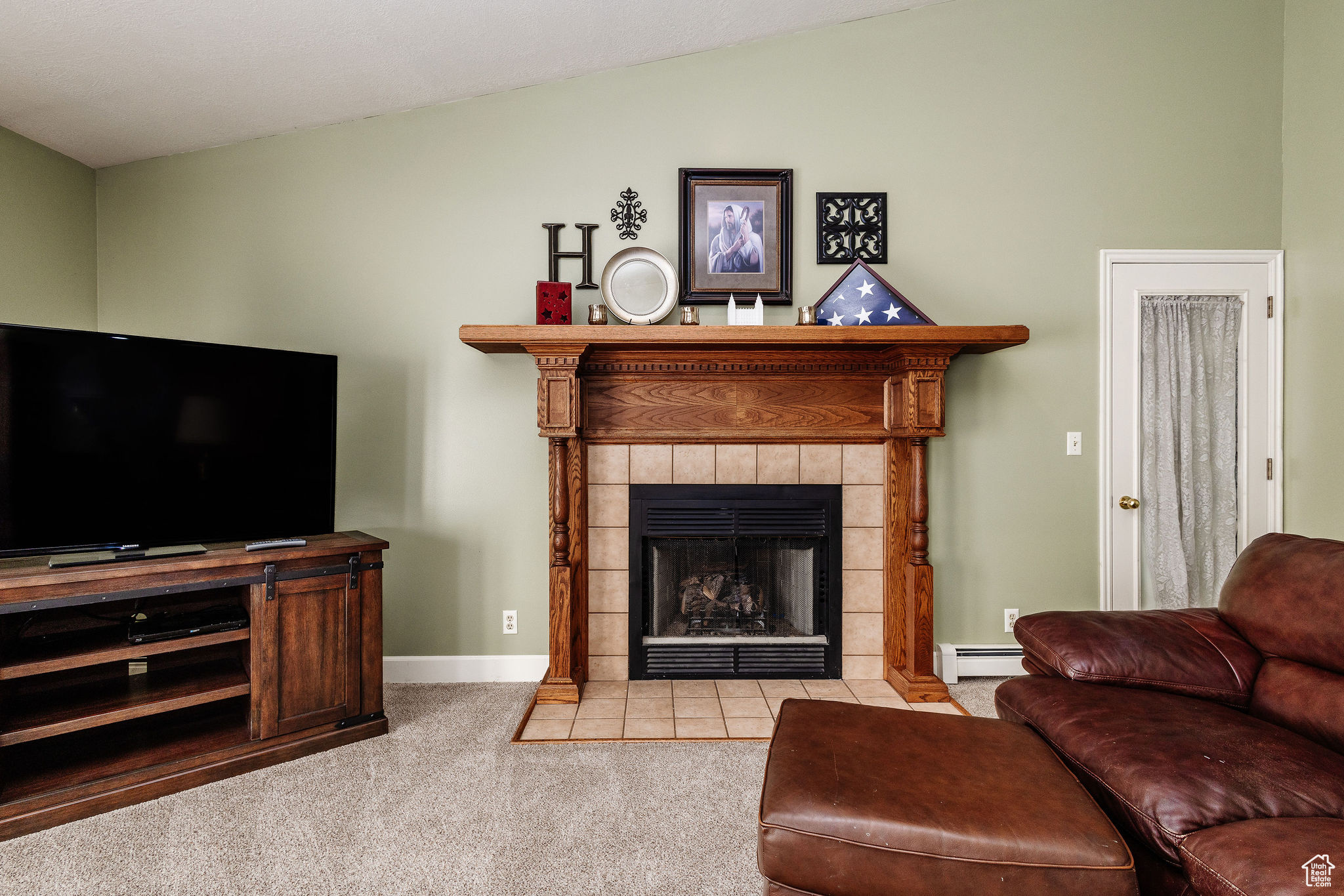 Carpeted living room with vaulted ceiling, a tile fireplace, and a baseboard heating unit