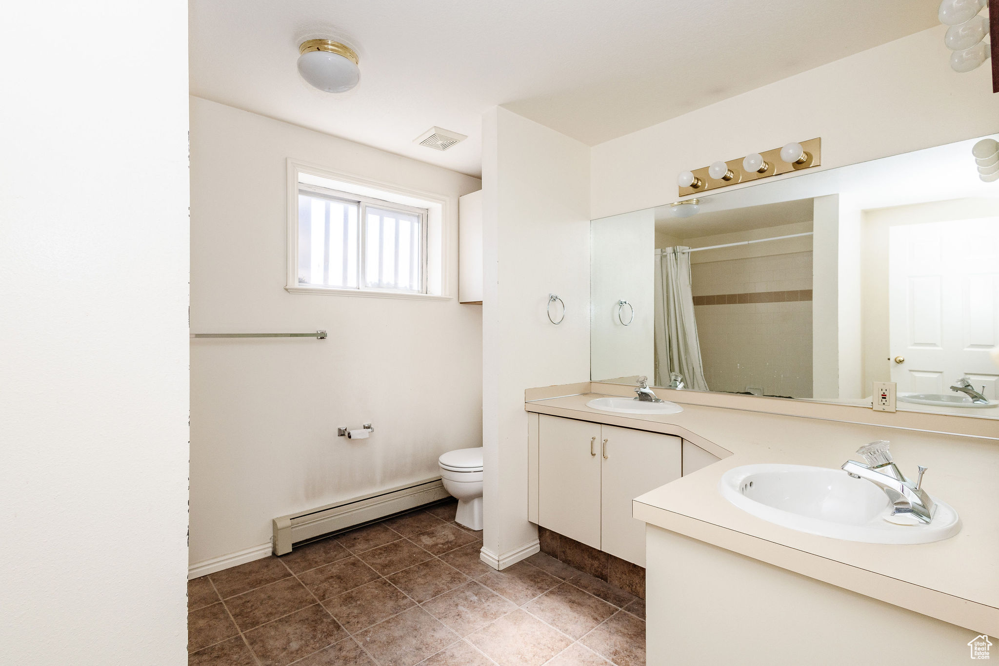 Bathroom featuring tile flooring, a baseboard heating unit, oversized vanity, double sink, and toilet