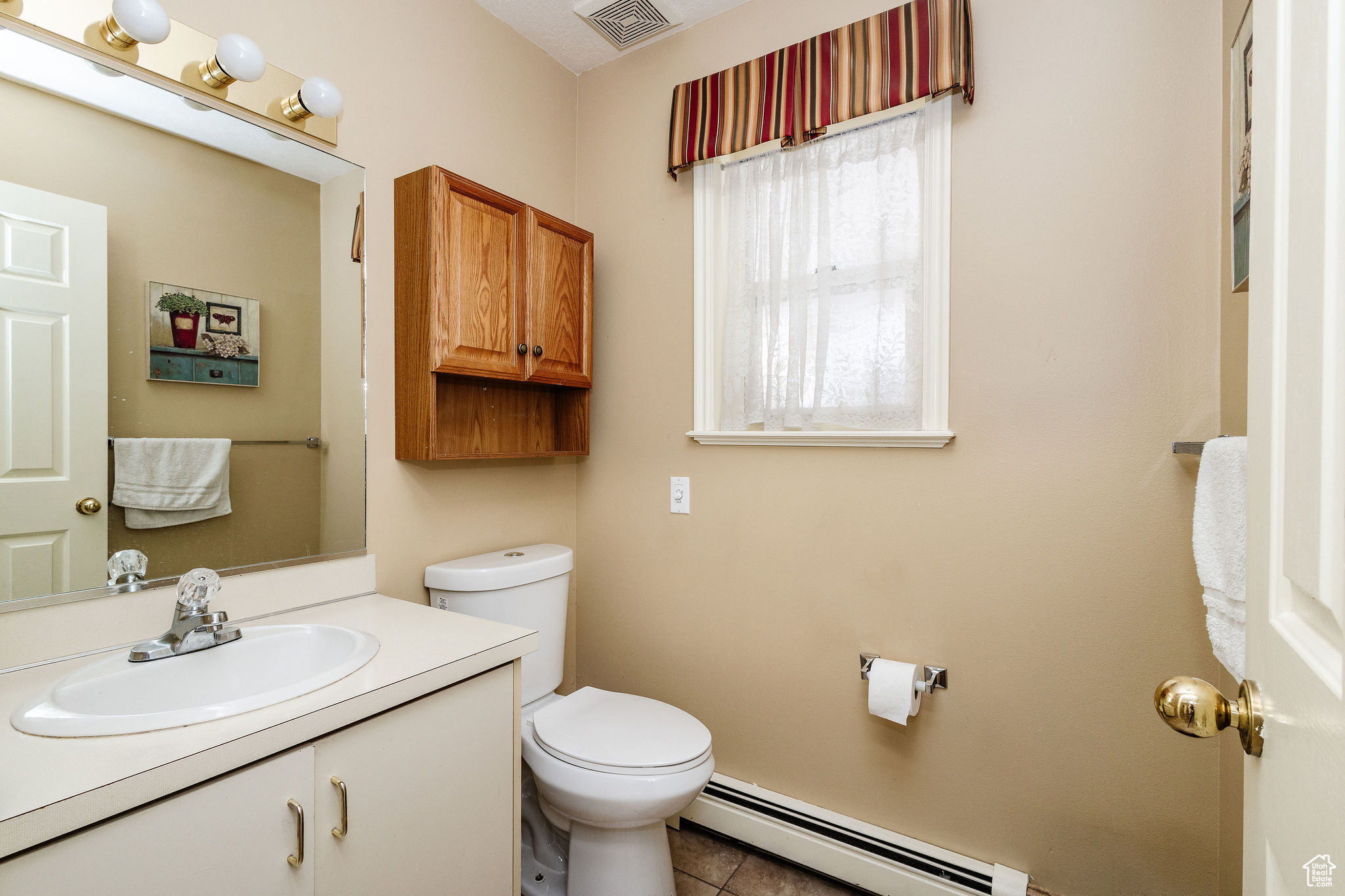Bathroom with baseboard heating, toilet, tile flooring, and large vanity