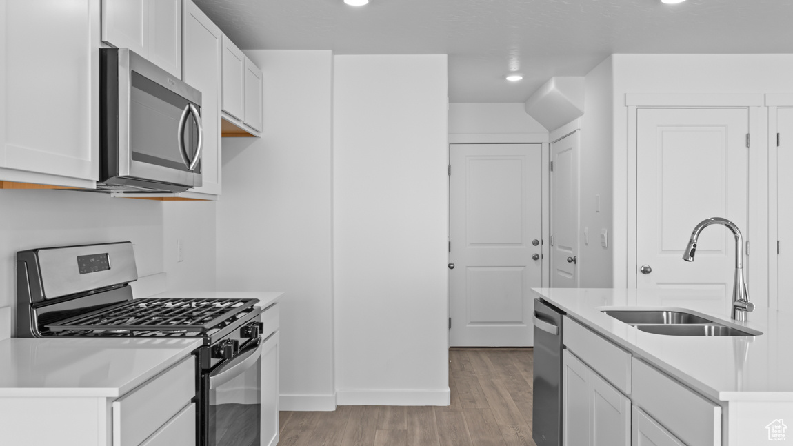 Kitchen featuring appliances with stainless steel finishes, sink, light wood-type flooring, and white cabinets