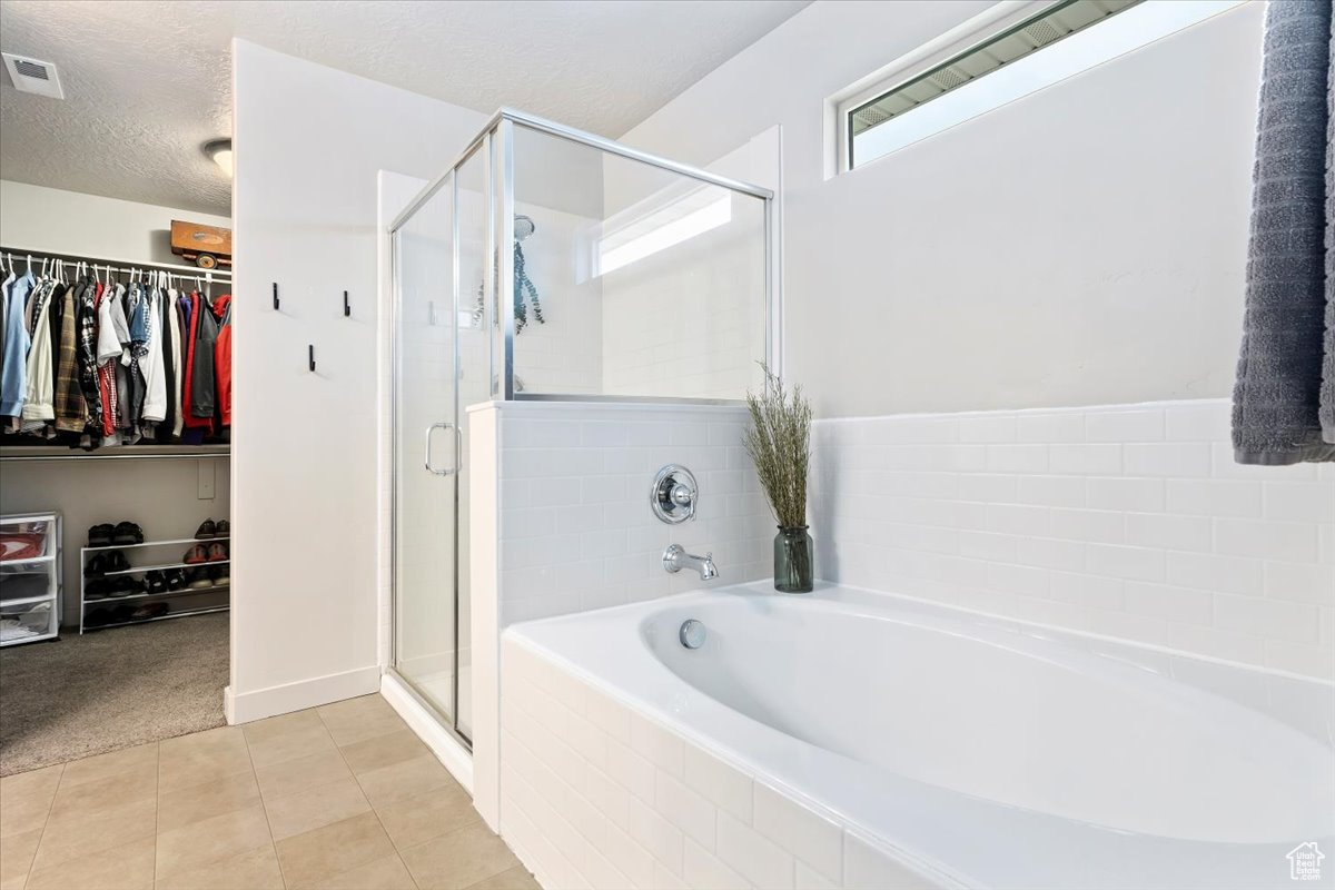 Bathroom with tile flooring, shower with separate bathtub, and a textured ceiling
