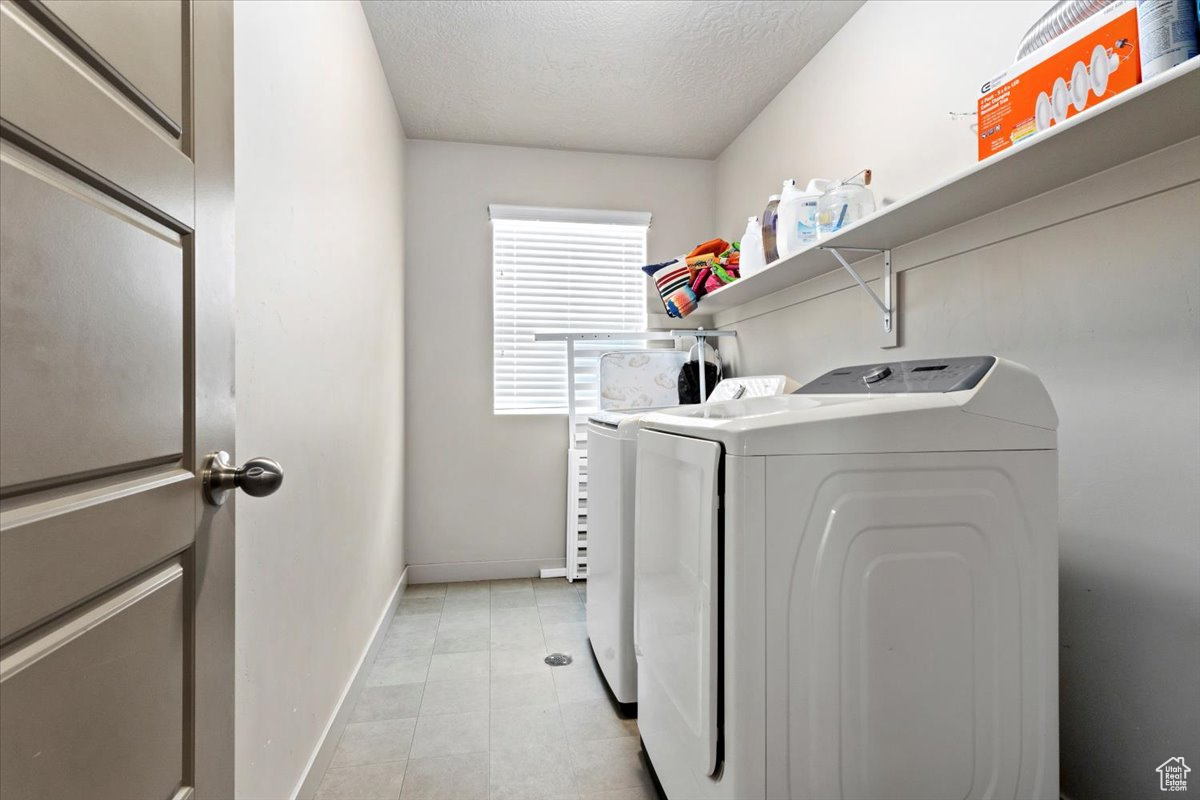 Washroom with a textured ceiling, washing machine and clothes dryer, and light tile floors