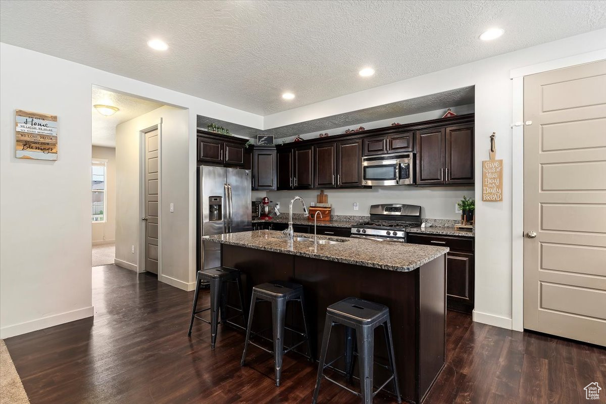 Kitchen with appliances with stainless steel finishes, dark hardwood / wood-style flooring, a kitchen bar, and an island with sink