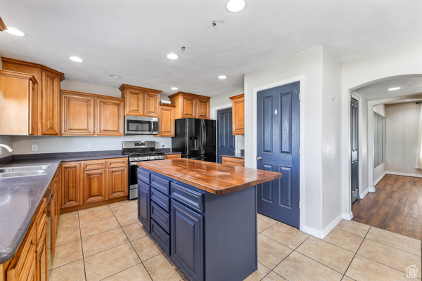 Kitchen featuring appliances with stainless steel finishes, light tile floors, a kitchen island, sink, and wood counters