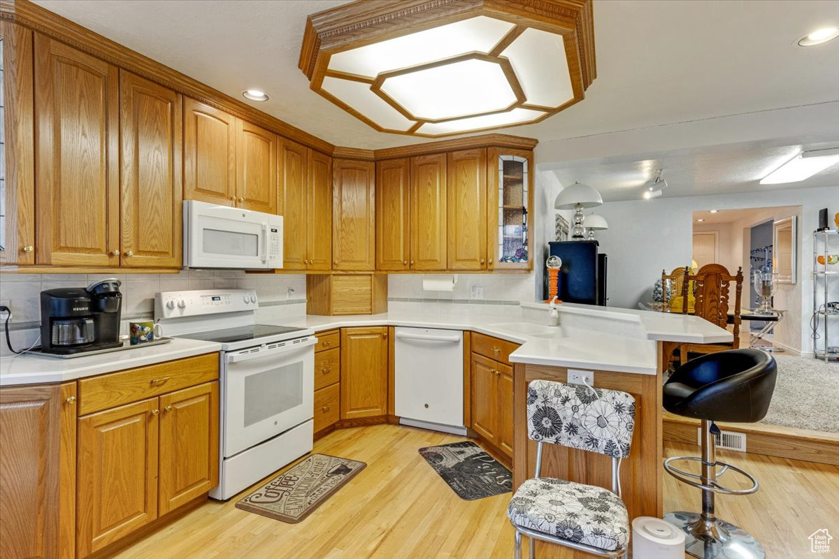 Kitchen featuring a kitchen breakfast bar, white appliances, light wood-type flooring, backsplash, and kitchen peninsula