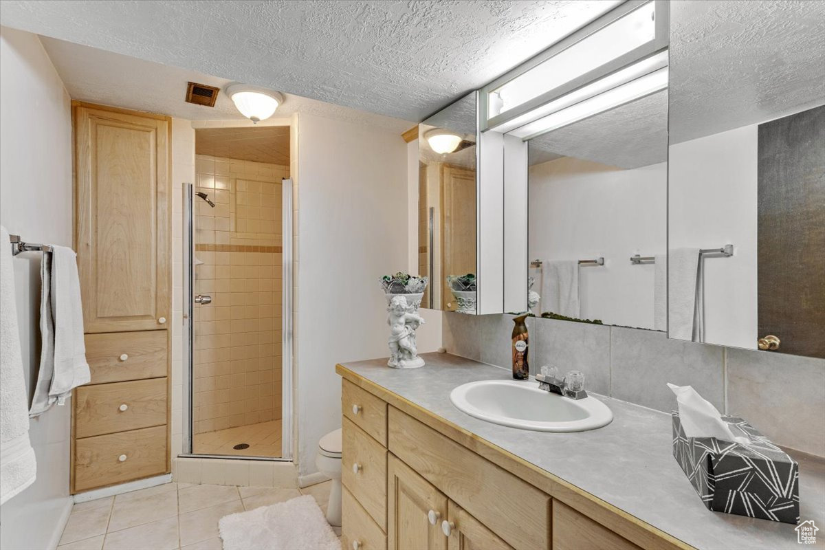 Bathroom featuring a shower with door, tile floors, large vanity, toilet, and a textured ceiling