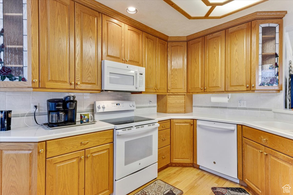 Kitchen featuring sink, white appliances, tasteful backsplash, and light wood-type flooring