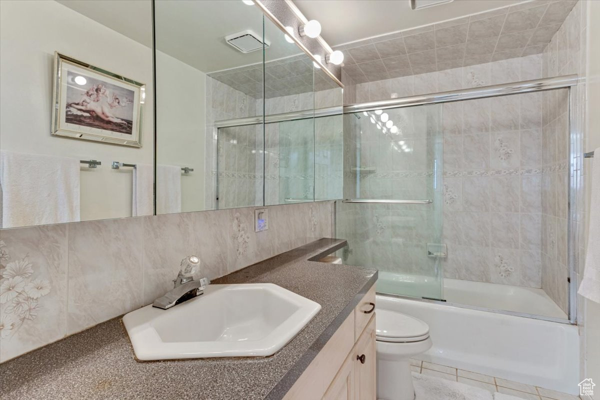 Full bathroom featuring tile walls, toilet, enclosed tub / shower combo, tile flooring, and vanity