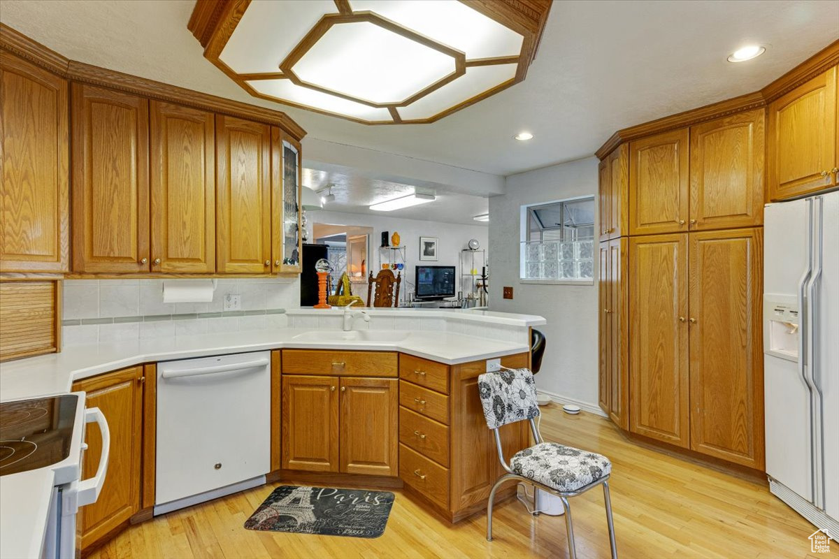 Kitchen featuring light hardwood / wood-style flooring, white appliances, tasteful backsplash, and kitchen peninsula