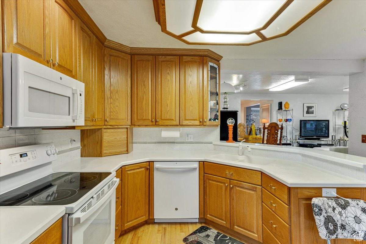 Kitchen with sink, white appliances, backsplash, and light wood-type flooring