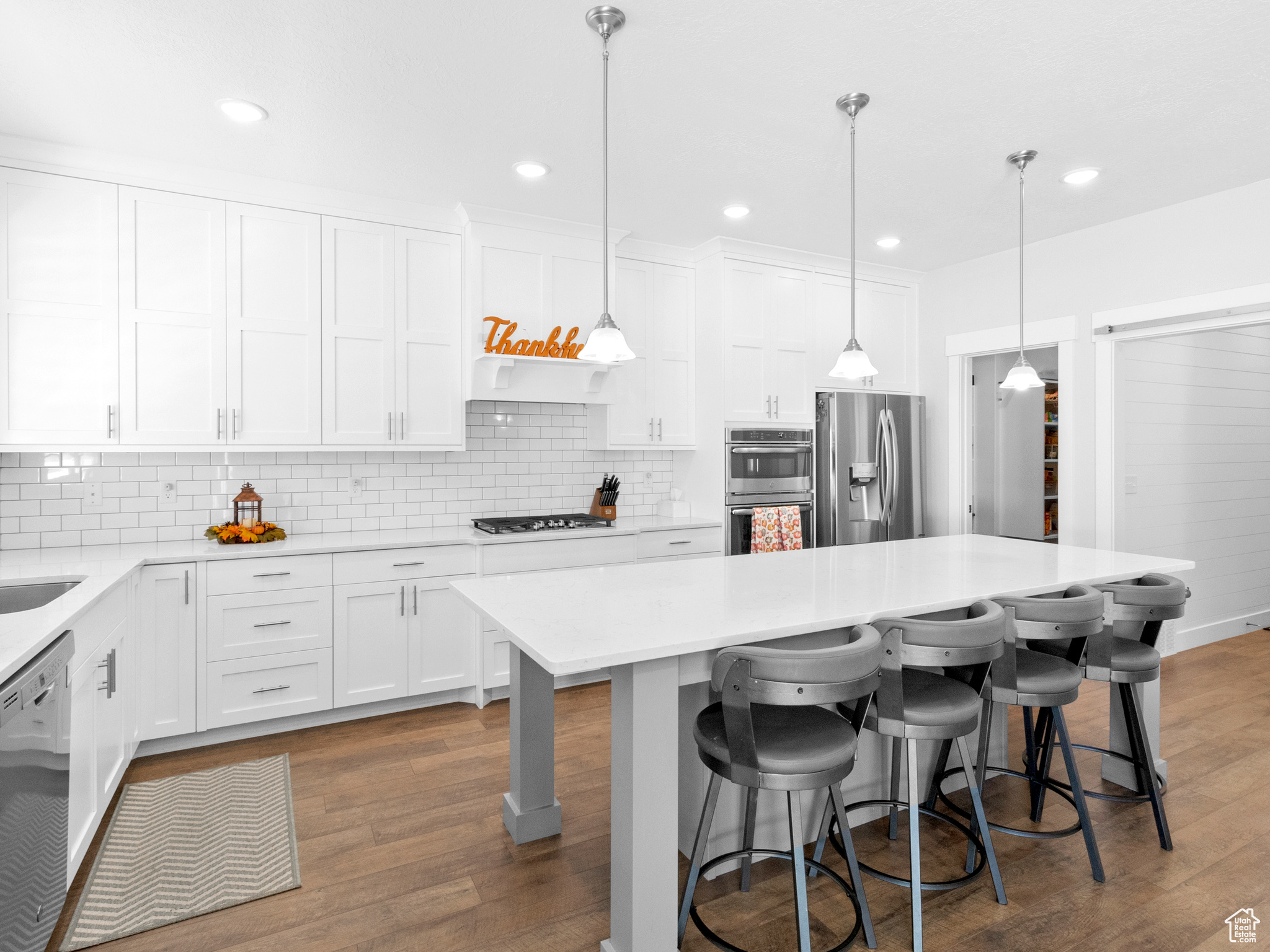 Kitchen featuring appliances with stainless steel finishes, tasteful backsplash, white cabinetry, hardwood / wood-style flooring, and a kitchen breakfast bar