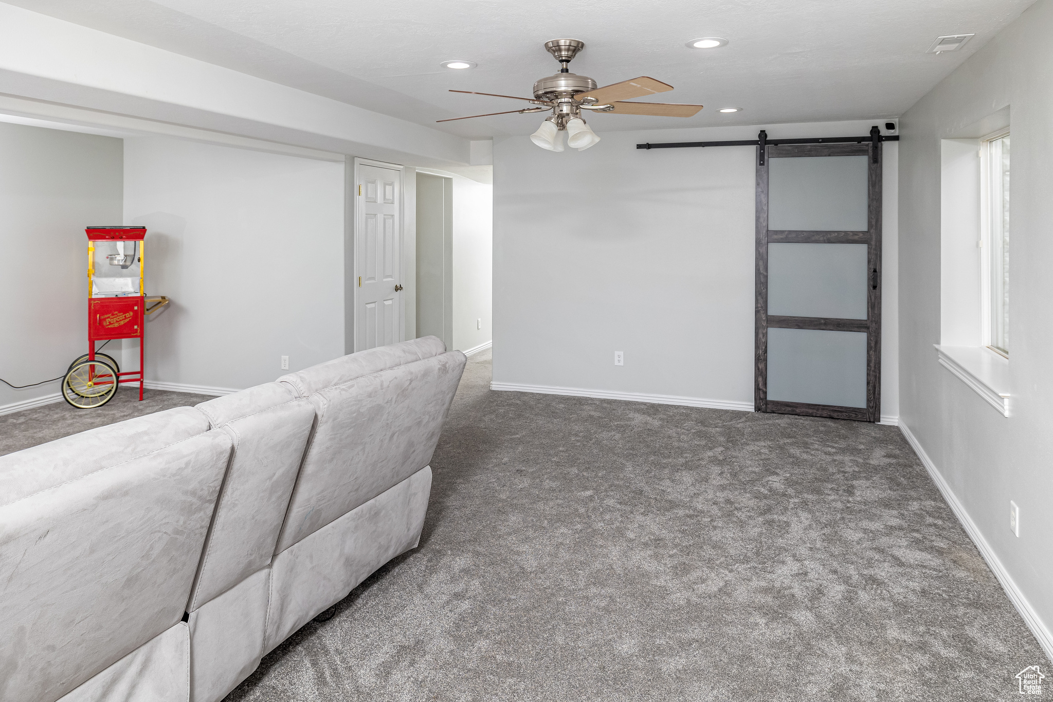 Living room featuring a barn door, ceiling fan, and dark carpet