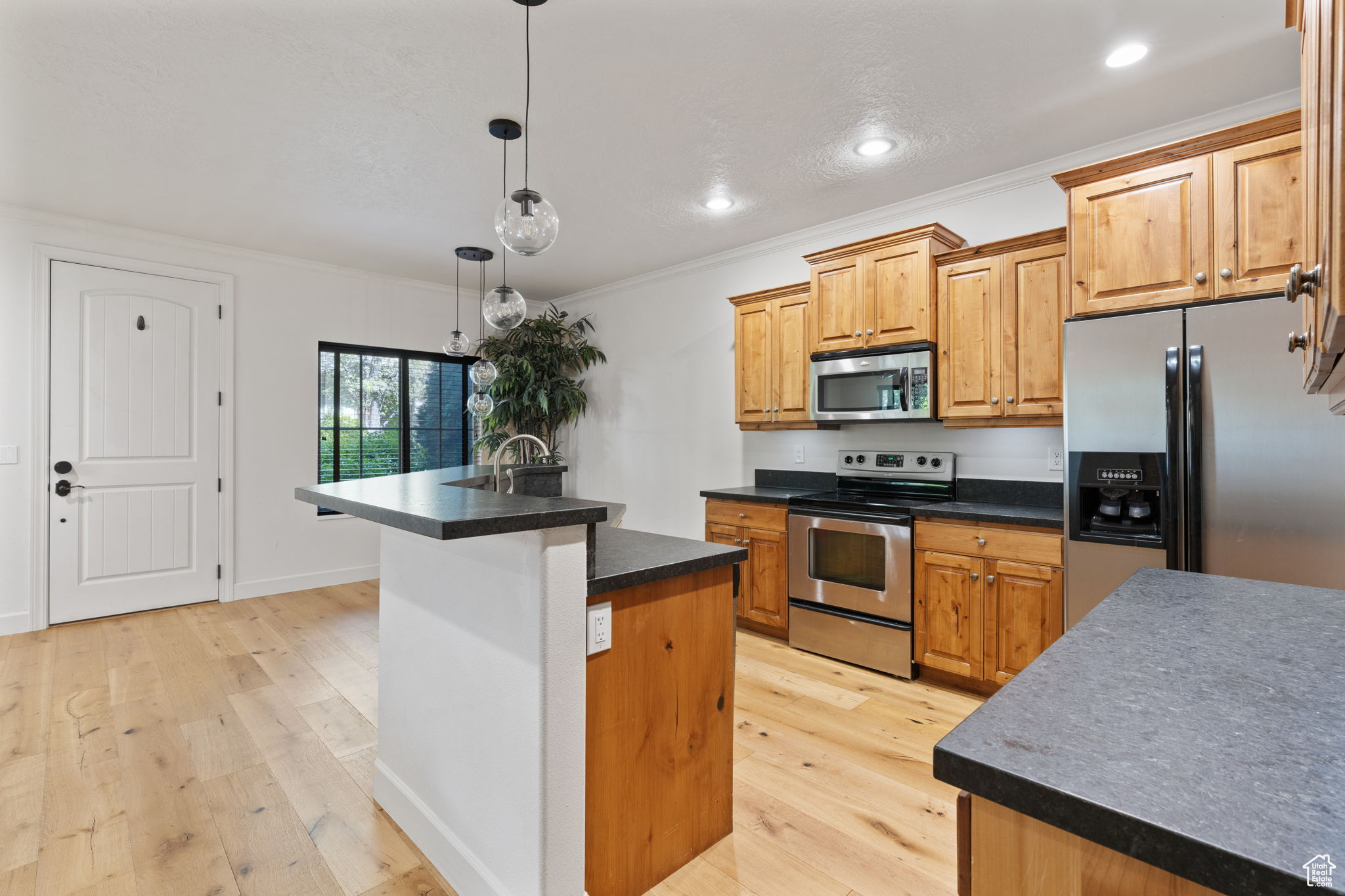 Kitchen featuring decorative light fixtures, light hardwood / wood-style flooring, stainless steel appliances, a center island with sink, and ornamental molding