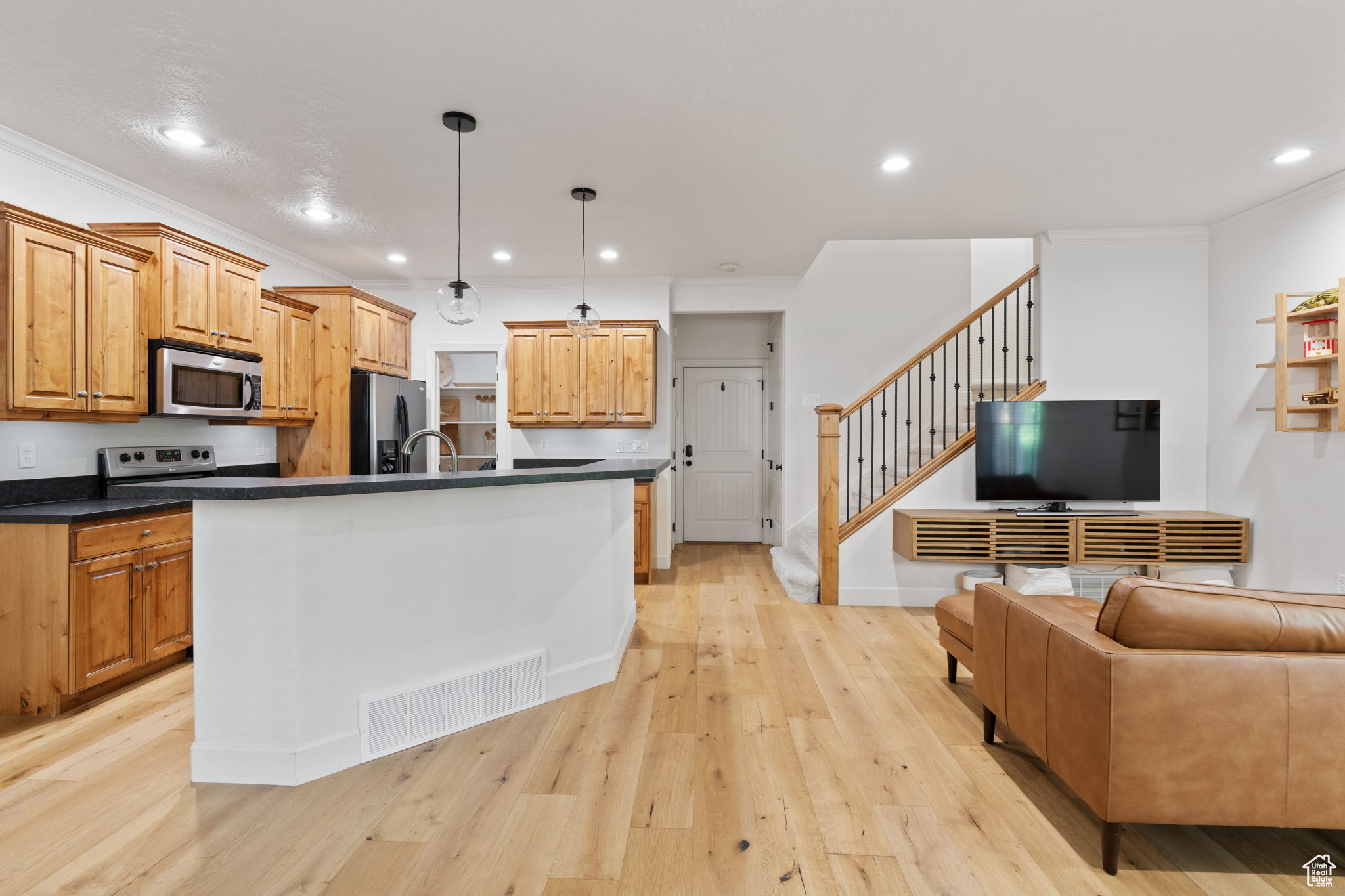 Kitchen with appliances with stainless steel finishes, light hardwood / wood-style flooring, pendant lighting, and crown molding