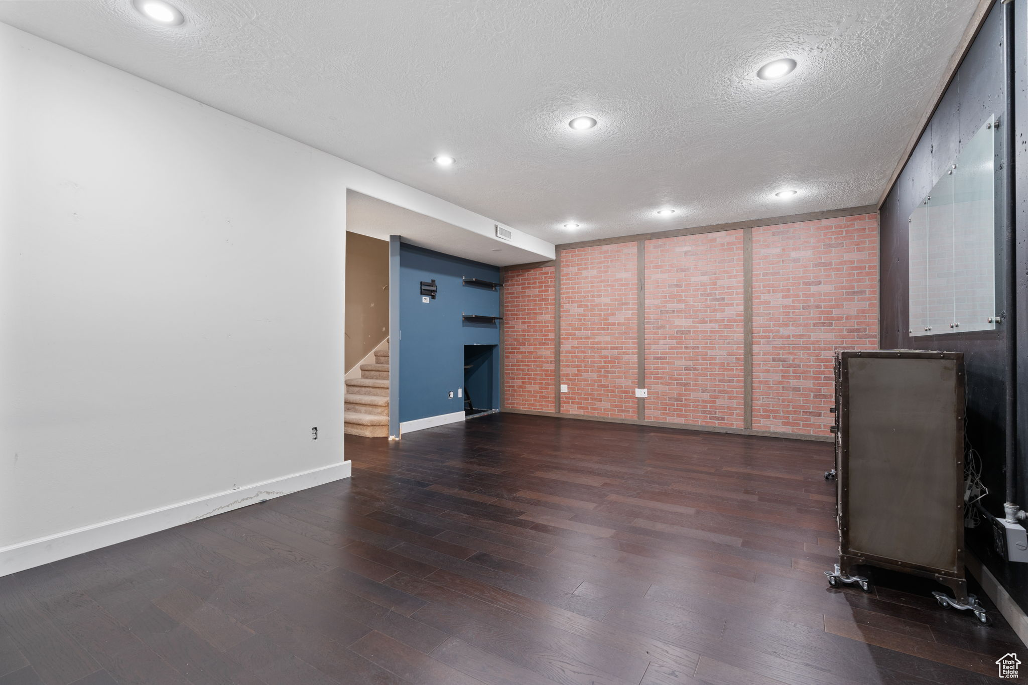 Unfurnished living room featuring brick wall, dark hardwood / wood-style floors, and a textured ceiling